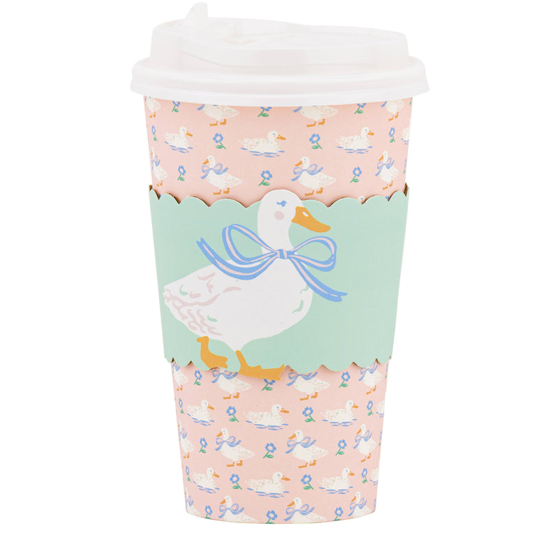 A single 16oz paper to-go cup featuring a pink duckling print, a mint green scalloped sleeve with a duck illustration, and a white plastic lid.