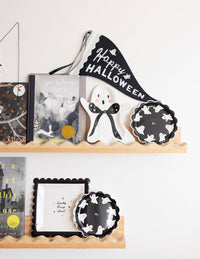 Halloween-themed decor items on a shelf including books, a ghost figurine, and decorative plates.
