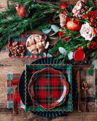 Holiday table setting with plaid plates, napkins, and red drink on wooden table