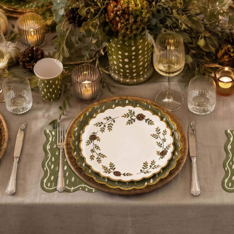 Fall place setting with an Evergreen Manor floral plate, olive dapple-dot cups, green scalloped napkins, candles, and a greenery centerpiece.