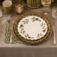 Fall place setting with an Evergreen Manor floral plate on an olive charger, a dapple-dot napkin, candles, and greenery.