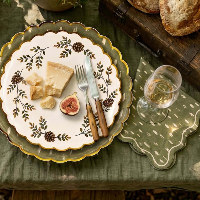 Place setting with an Evergreen Manor pinecone plate layered on the olive dapple-dot plate, cheese and figs, gold cutlery, and a matching napkin.