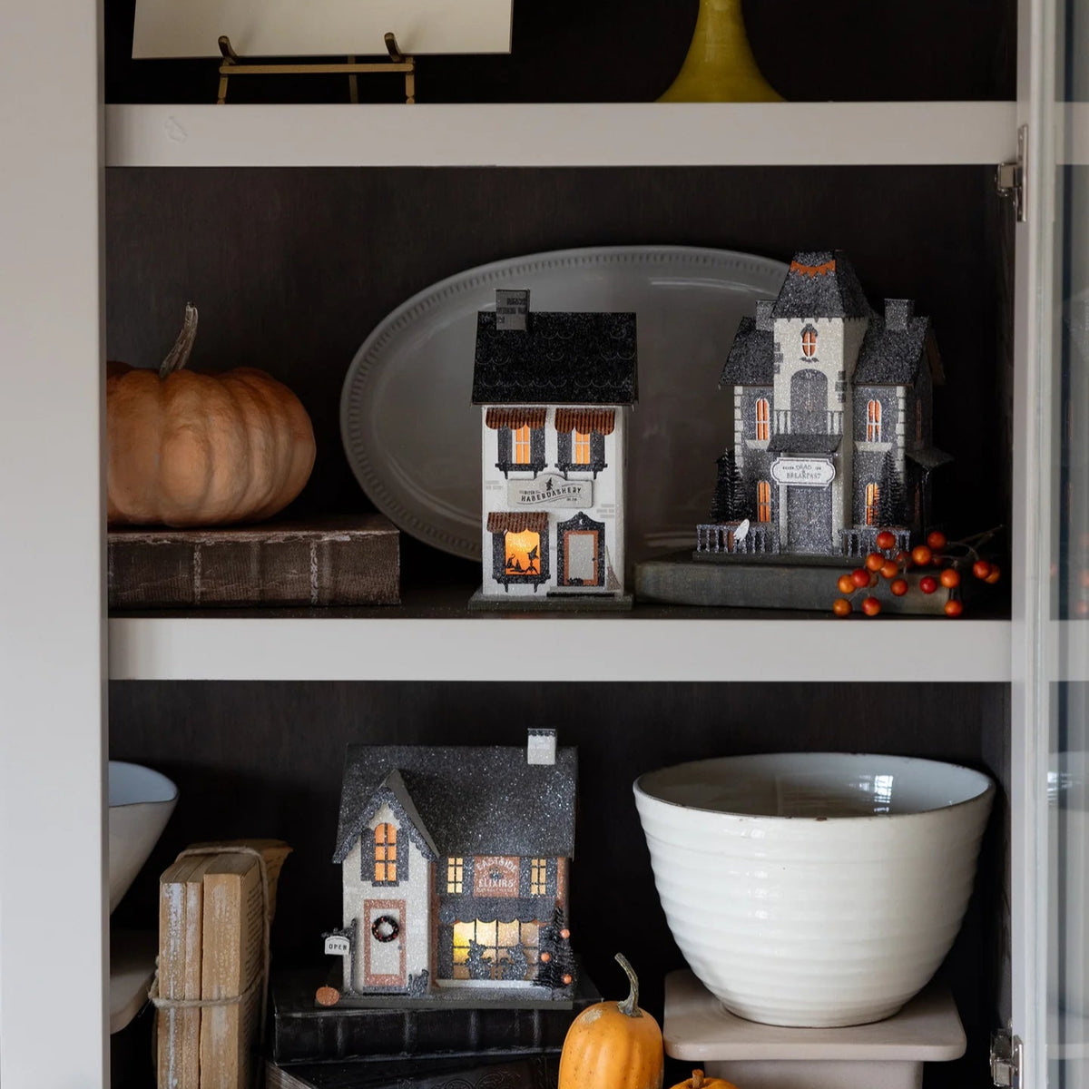 Grouping of light-up Halloween village houses on a cabinet shelf; Dead & Breakfast shown with coordinating pieces.