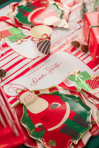 Kids’ craft setup with cups, snow, and pinecones around scroll placemats.