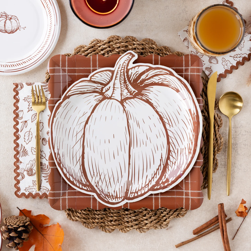 A fall table setting with a pumpkin-shaped plate on a brown plaid placemat and woven charger.