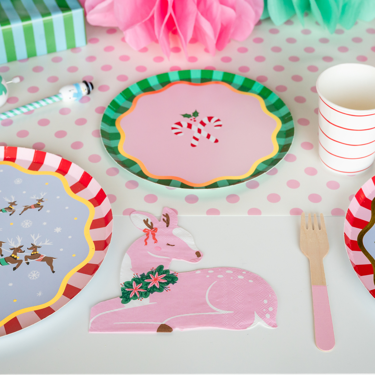 Pink deer napkin at a kids Christmas place setting with candy cane and Santa plates and a pink wooden fork