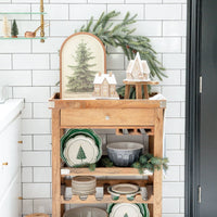 Close-up of the Evergreen serving platter on a wood cart with gingerbread houses and matching green Christmas Lane Collection plates.