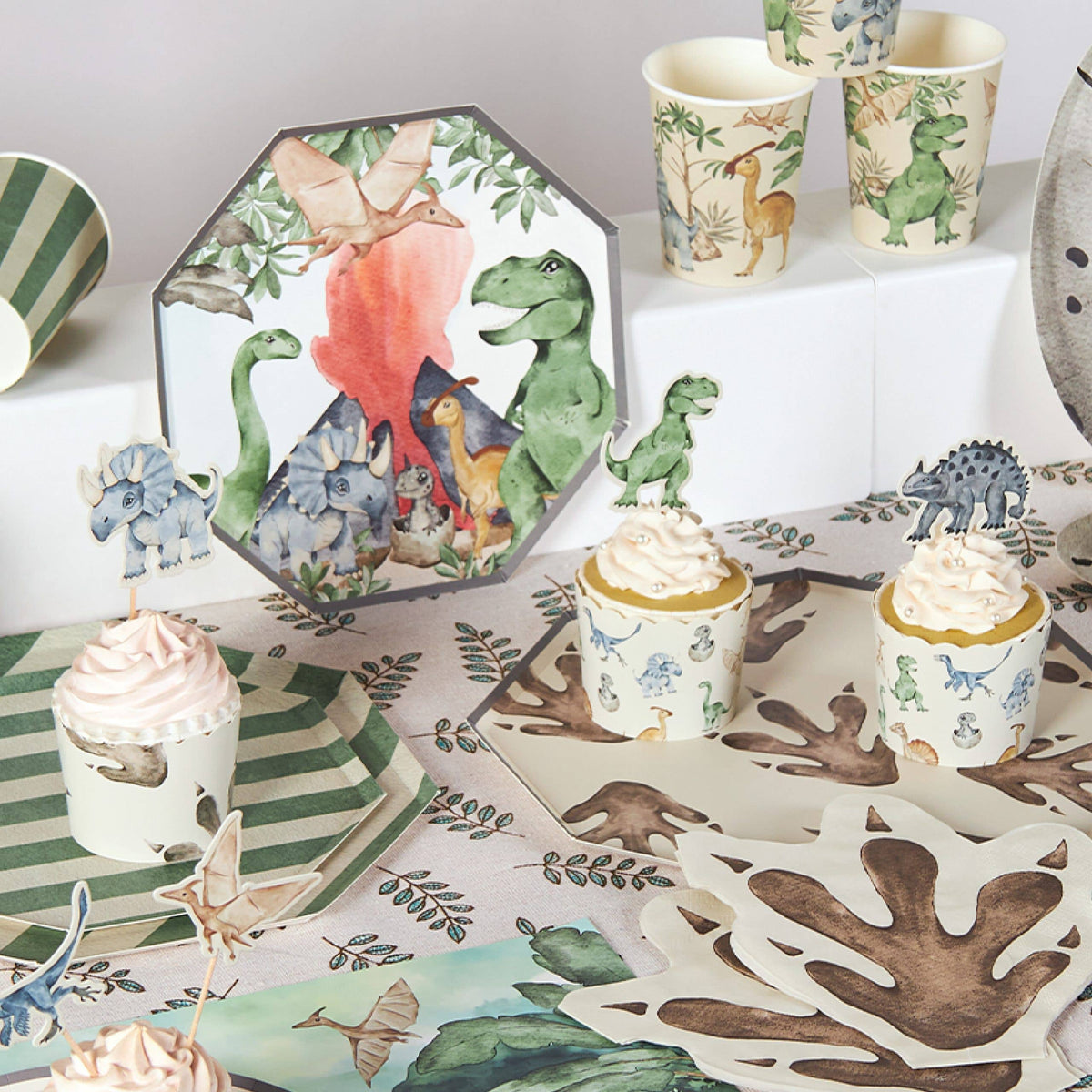 Alt Text: Table setting with dinosaur plates, cups, and cupcakes with dinosaur toppers