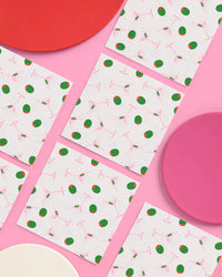 Martini print paper cocktail napkins arranged in a grid with pink and red plates on a pink background