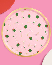 Multiple pink martini print paper plates arranged on pink background with red and white plates showing gold foil rim detail and martini olive pattern
