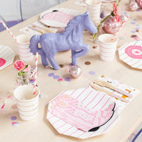 Overhead shot of a pale-wood table set for a cowgirl gathering: pink boot napkins on striped plates, horse-print napkins, pink disco balls, and wood-fork place settings.