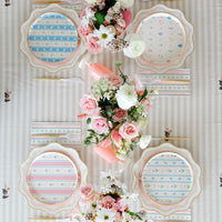 Overhead Easter brunch table with four pastel plate designs, pink vases, gold cutlery and pink floral centerpiece on striped linen