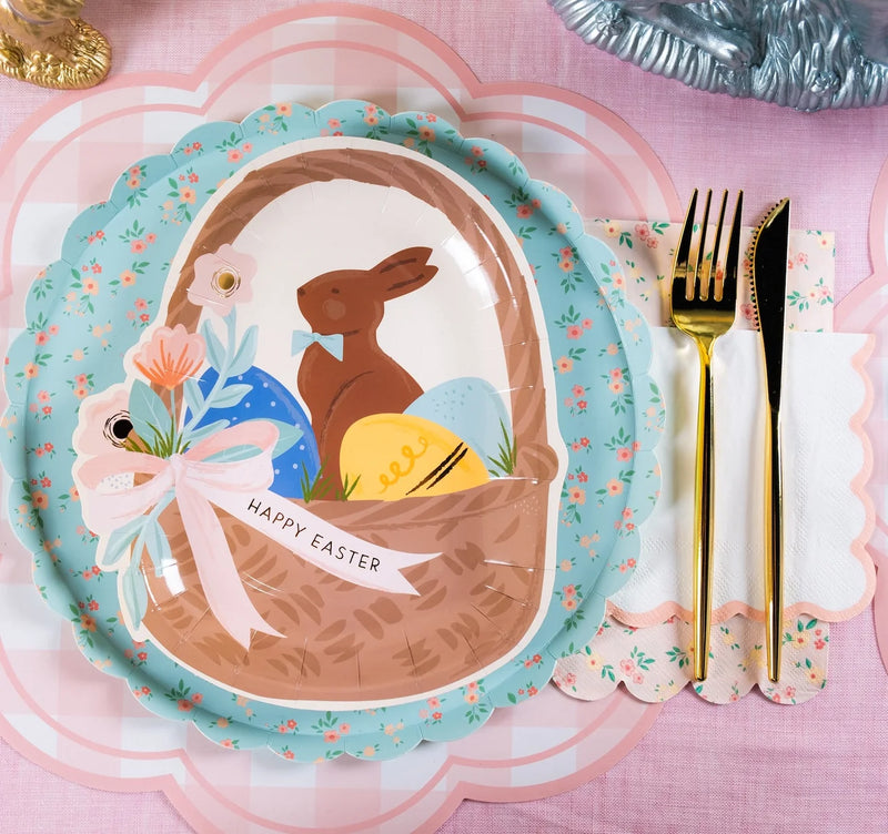 Easter place setting with an egg-shaped chocolate bunny basket plate, blue floral scalloped plate, pink gingham plate, floral napkin, and gold flatware