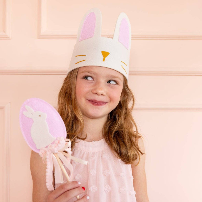 A young girl wearing a white felt bunny crown and holding a bunny wand, styled for an elegant backyard Easter egg hunt.