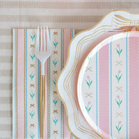 Pink and blue striped Easter plate stacked on scalloped dinner plate with matching napkin, white fork and gold cutlery on linen tablecloth