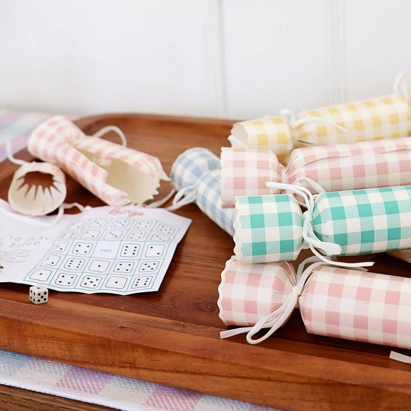 A wooden tray filled with pastel gingham party crackers, showing an open cracker with a "Dice Bingo" game card, a pencil, and a die