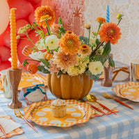 Pumpkin vase centerpiece with candles; gingham dinner plate and gold flatware at each setting.