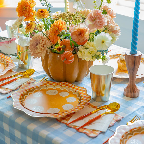 Fall tablescape with gingham orange napkins, gold flatware, and pumpkin centerpiece.