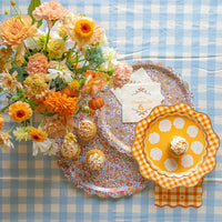 Top-down shot of blue gingham table with floral trays, cupcake, and Thanksgiving napkins in orange plaid.