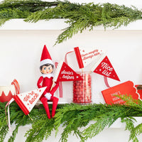 Elf on the Shelf holiday scene with mini felt pennant flags and Christmas greenery on a shelf.