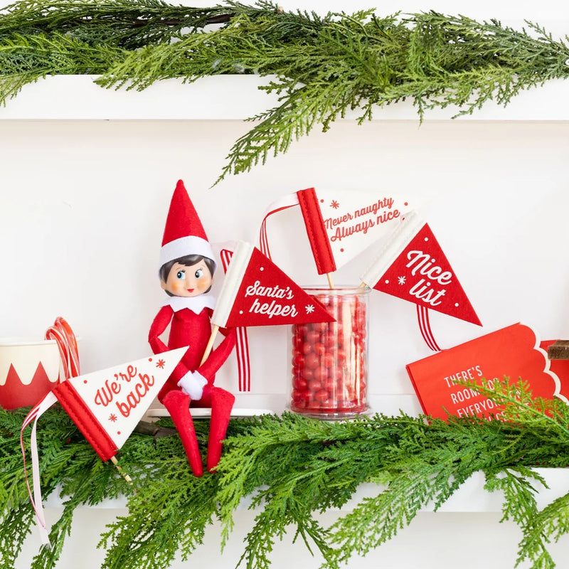 Elf on the Shelf holiday scene with mini felt pennant flags and Christmas greenery on a shelf.