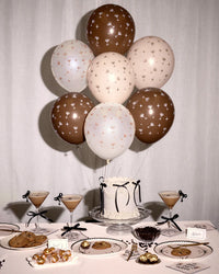 Bouquet of espresso martini print latex balloons in brown, cream, and blush floating above a styled party table with espresso martini cocktails, a white cake, and cookies