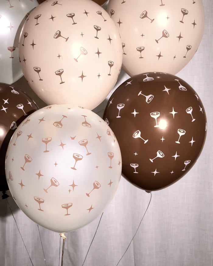 Close-up cluster of espresso martini coupe print balloons in blush, cream, and chocolate brown against a white linen backdrop