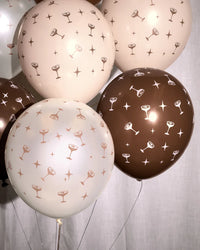 Close-up cluster of espresso martini coupe print balloons in blush, cream, and chocolate brown against a white linen backdrop