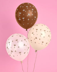 Three matte latex balloons in chocolate brown, blush pink, and cream with an all-over espresso martini coupe and star print, floating against a pink background