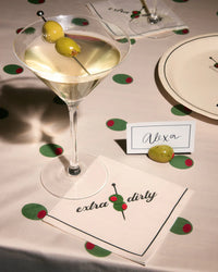 Extra dirty martini napkin under a cocktail glass on a styled tablescape with place card and olive confetti