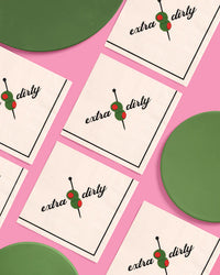 Extra dirty martini cocktail napkins arranged in a grid pattern with green plates on a pink background
