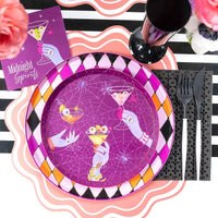 Layered Halloween place setting showing the Midnight Spirits plate on a striped table runner next to black plastic cutlery and a pink scalloped napkin.