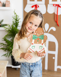 Child holding a Gingerbread Man Plate and smiling during a holiday table setup.