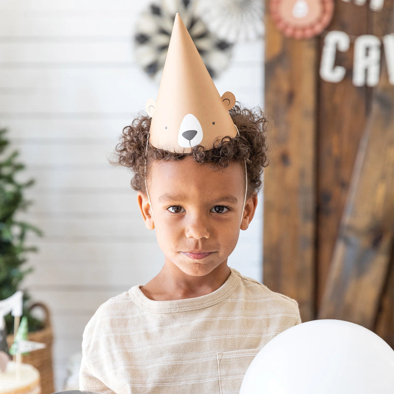 Birthday child wearing a bear hat and holding a balloon, styled with forest-inspired decorations in the background.