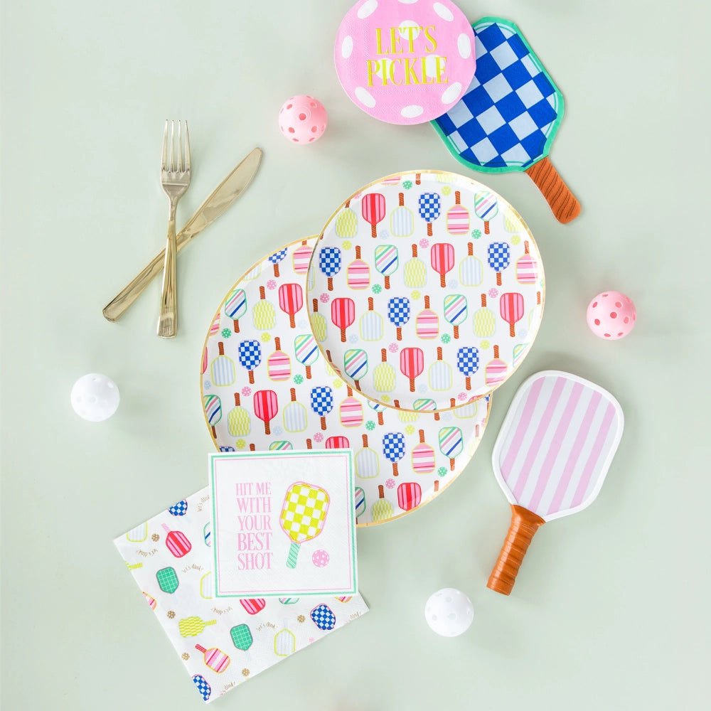 Tabletop flat lay of matching pickleball plates, napkins, and balls alongside gold cutlery.
