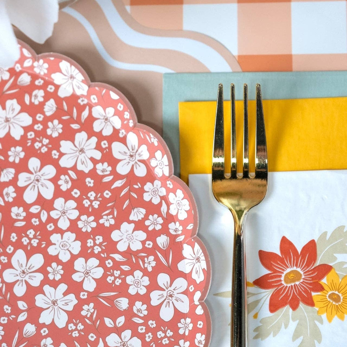 Rust floral scalloped plate beside a gold fork, yellow and sage napkin, and peach gingham runner