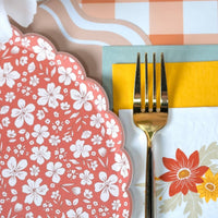 Rust floral scalloped plate beside a gold fork, yellow and sage napkin, and peach gingham runner