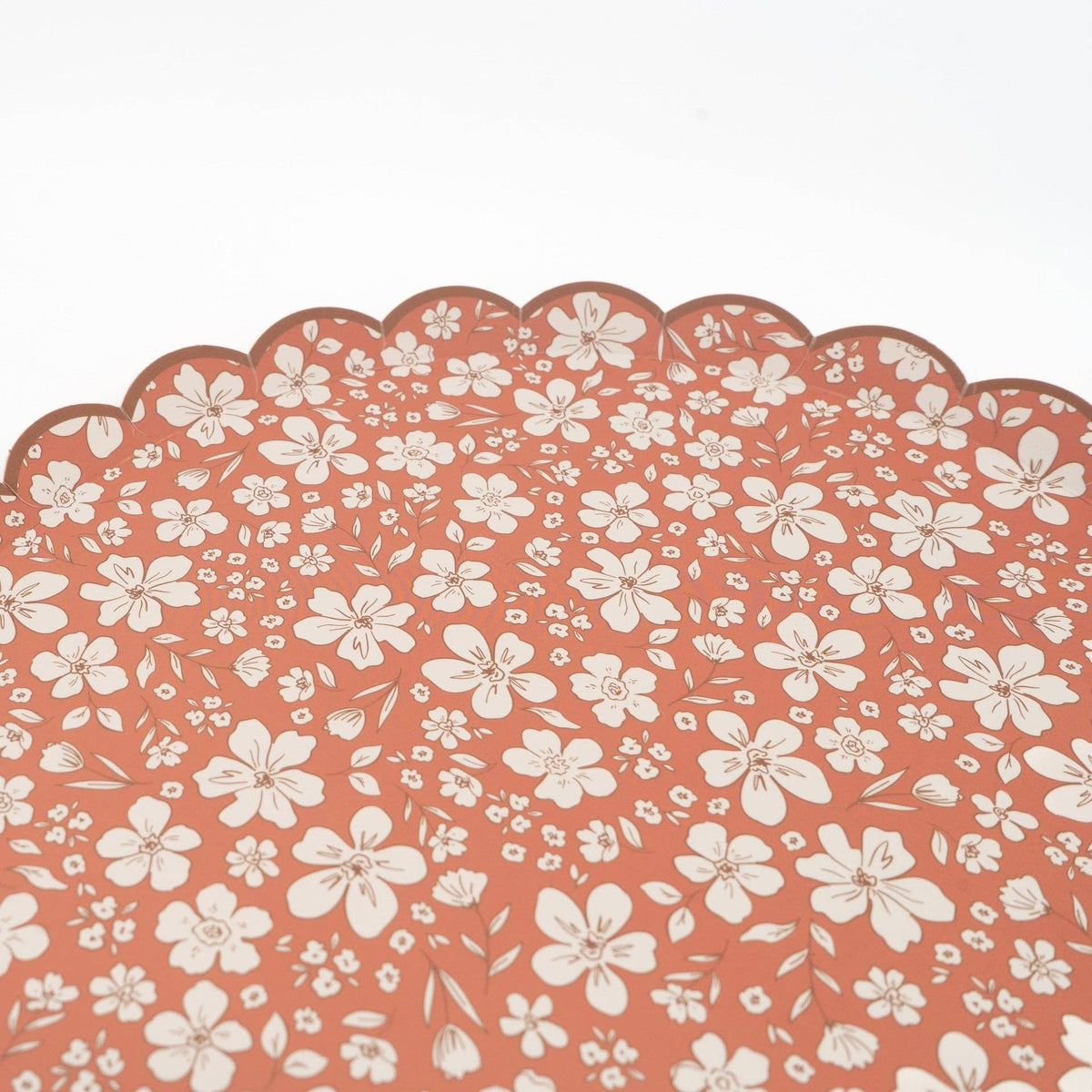 Detail of the scalloped rim and cream floral pattern on a terracotta paper plate
