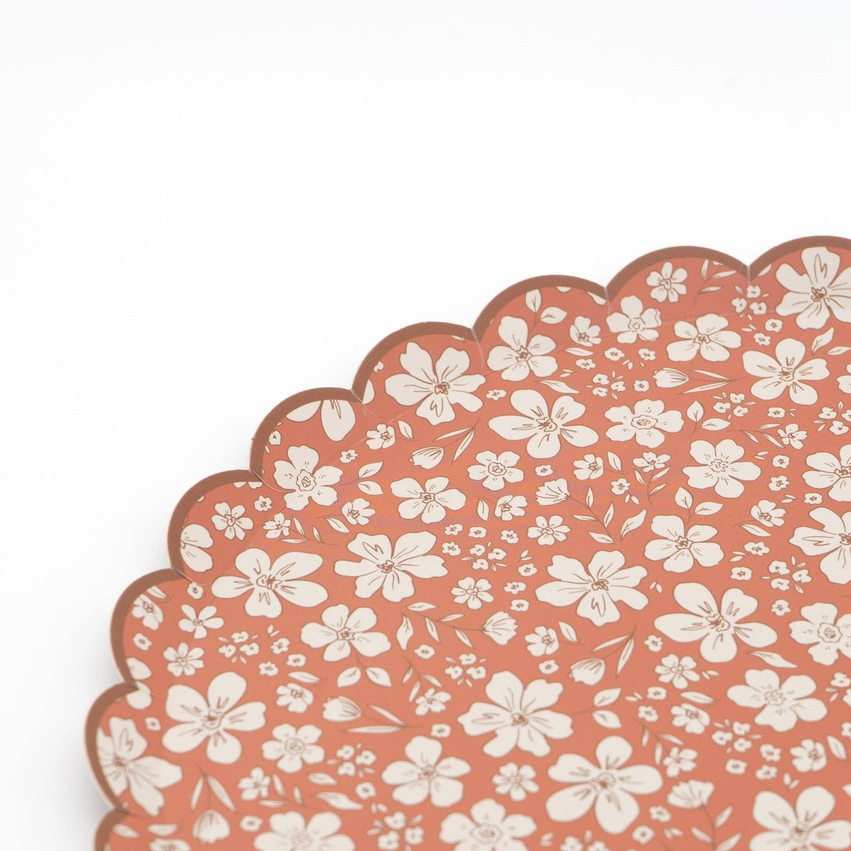Close crop of the scalloped edge and cream flower print on the rust paper dinner plate
