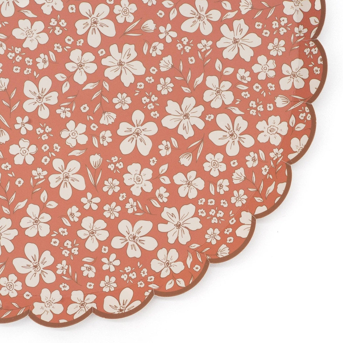 Close crop of the scalloped edge and cream flower print on the rust paper dinner plate
