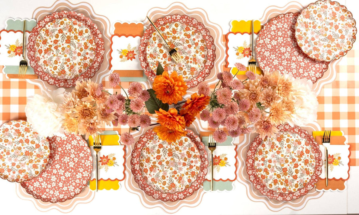 Six place settings with fall floral scalloped dinner plates, gold flatware, and pink and orange mums