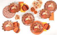Fall floral scalloped plate alongside turkey shaped plates and pumpkin napkins in a Thanksgiving flat lay