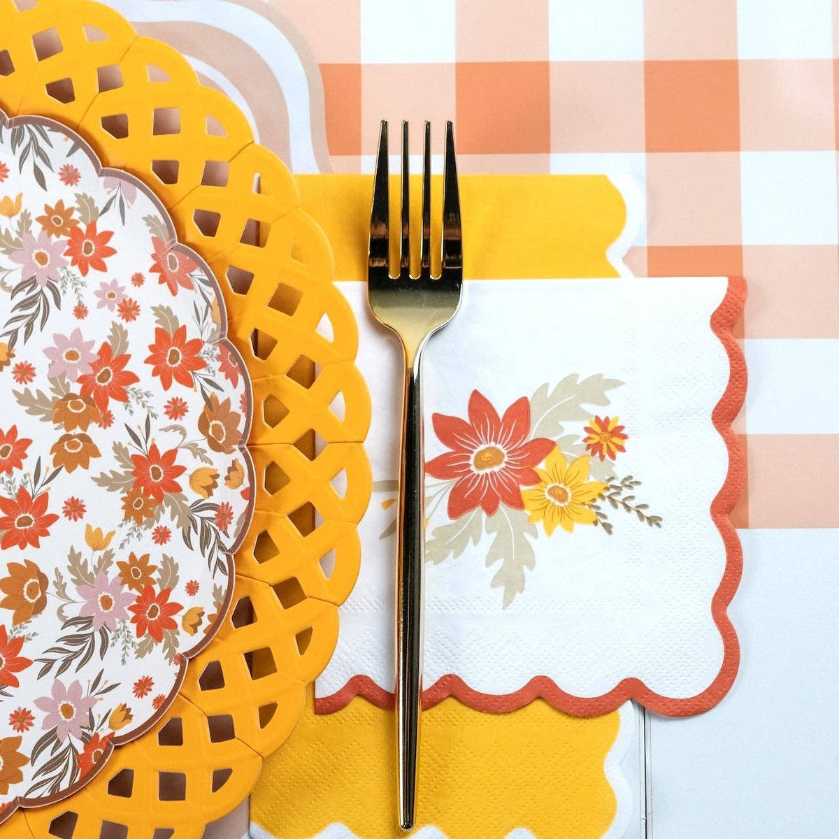 Fall floral plate on a marigold lattice charger beside a gold fork and scalloped napkins on peach gingham