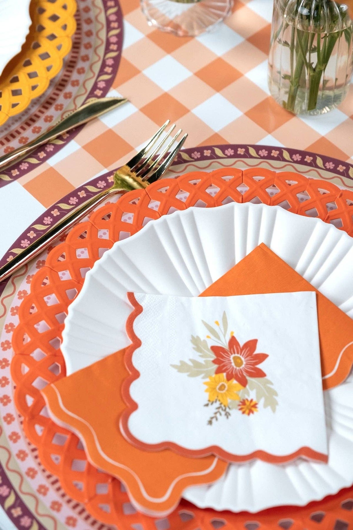 Close-up of a fall floral napkin on an orange napkin and white pleated plate over an orange lattice charger