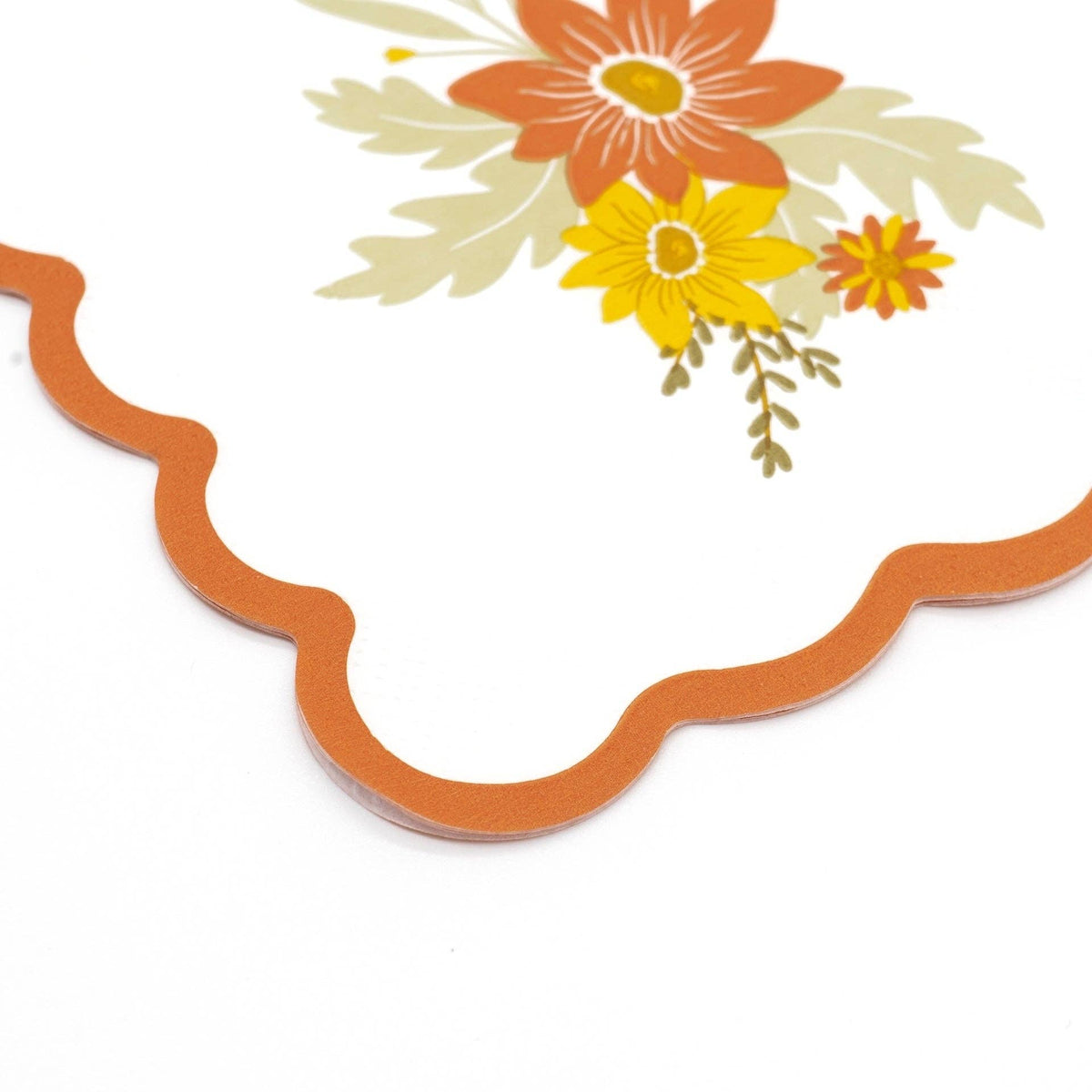 Corner detail of the rust scalloped edge on a fall floral paper napkin