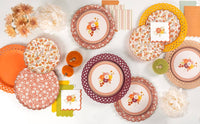 Flat lay of a fall party collection with floral plates, lattice chargers, scalloped napkins, and velvet pumpkins