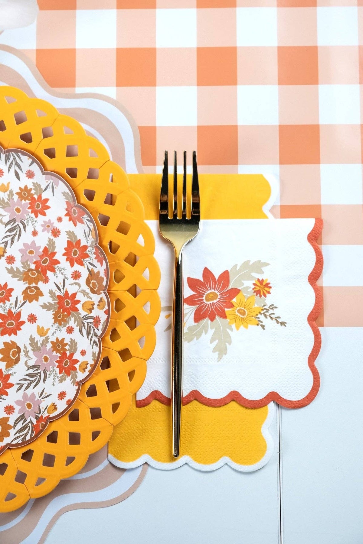 Fall floral napkin layered over a yellow guest towel beside a marigold lattice charger on peach gingham
