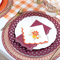 Styled fall place setting showing the burgundy napkin with a white floral plate on a burgundy basketweave charger over a gingham runner.