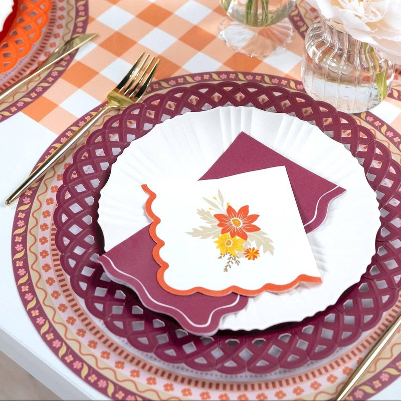 Styled fall place setting showing the burgundy napkin with a white floral plate on a burgundy basketweave charger over a gingham runner.