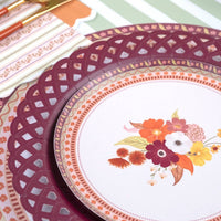 Styled fall place setting showing the burgundy plate layered under a white floral salad plate with a burgundy napkin and autumn florals.